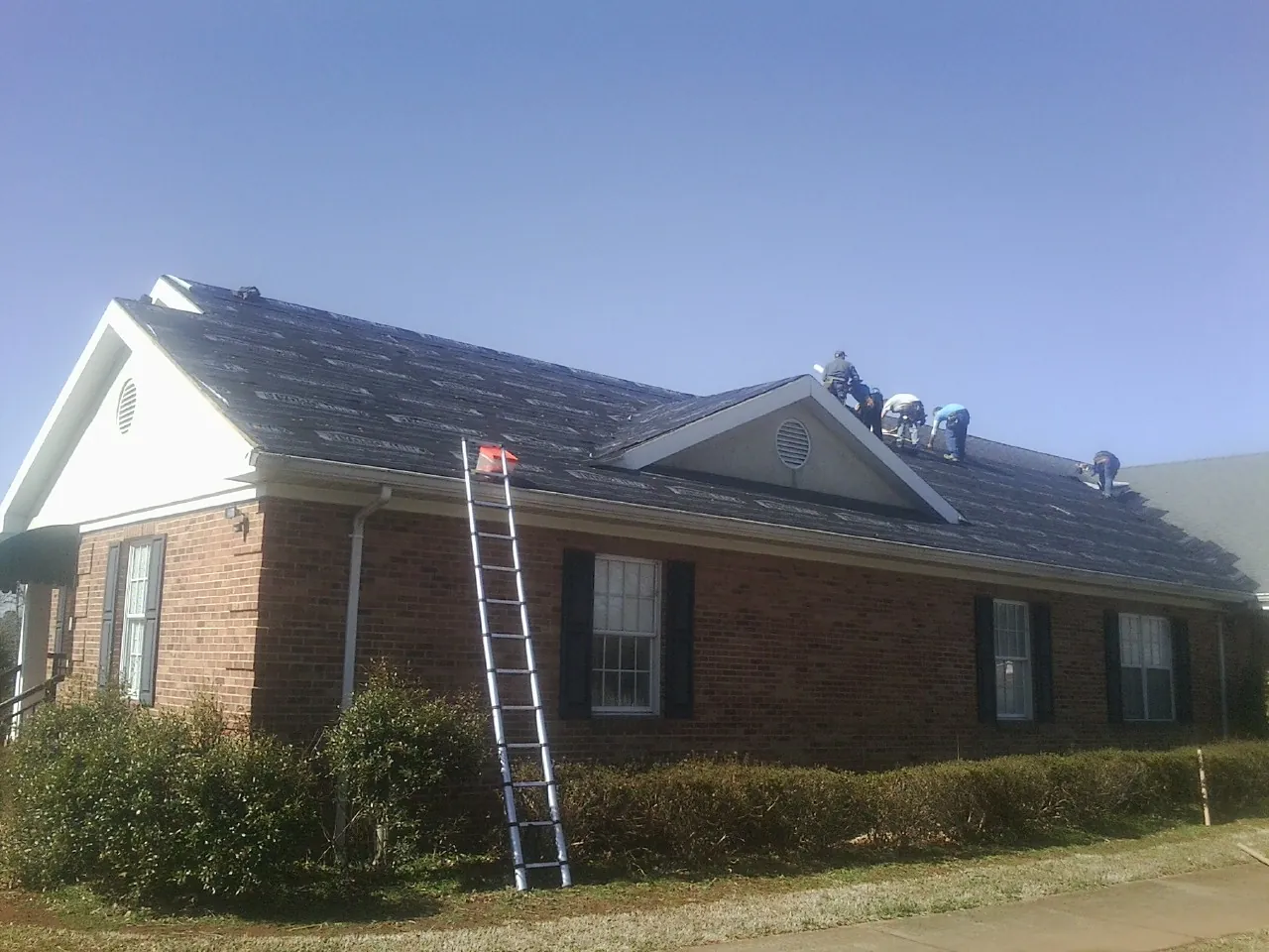 Crew tearing shingles off a brick ranch roof with a ladder set — Emergency Roof Repair work by our crew in Birds Landing