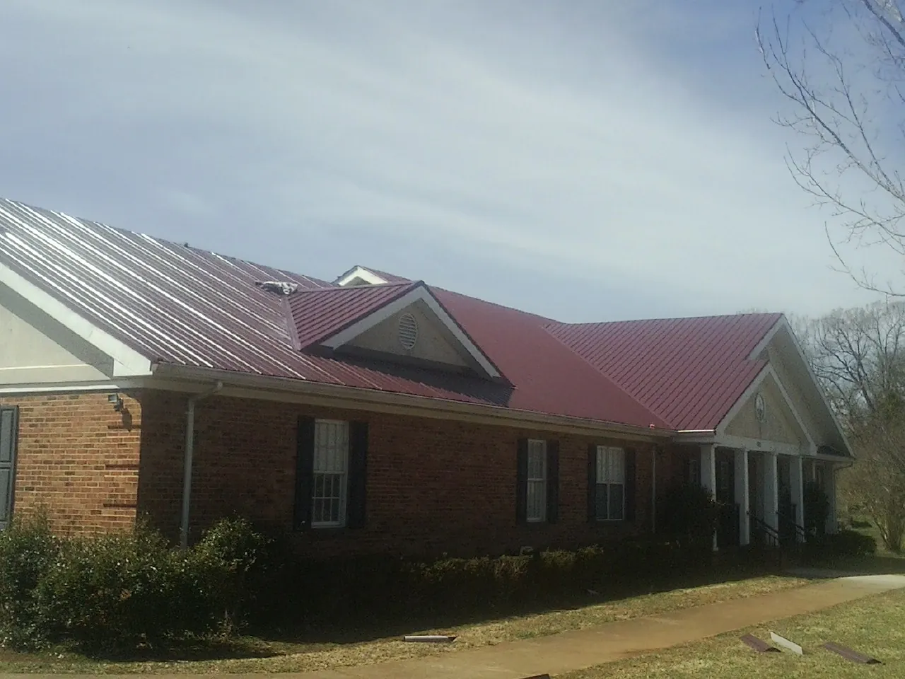 Red metal roof with gabled entries on a long brick building, from a Hail Damage Roof Repair job in Birds Landing