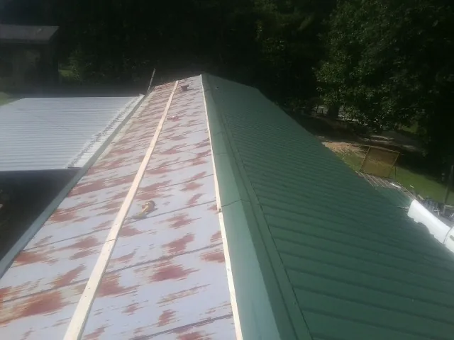 Old rusted panels beside newly installed green metal roofing — Wind Damage Roof Repair by Roofing Brothers in Birds Landing