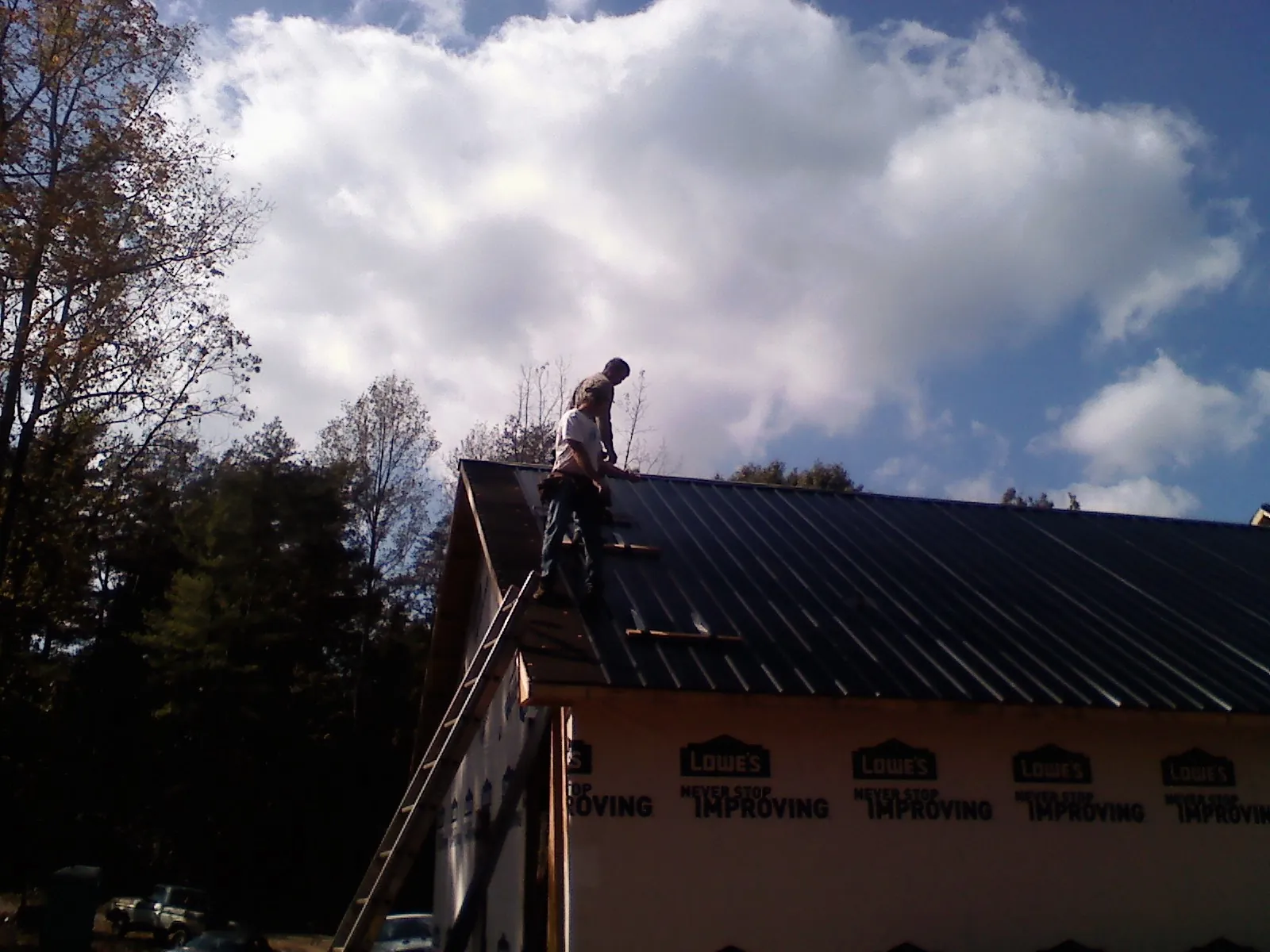 Roofer fastening dark metal panels high against a cloudy sky, from a Roof Inspection job in Birds Landing