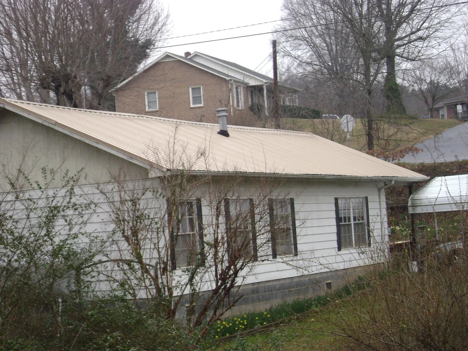Tan metal roof on a white sided house set into a hillside — Commercial Roofing by Roofing Brothers in Birds Landing